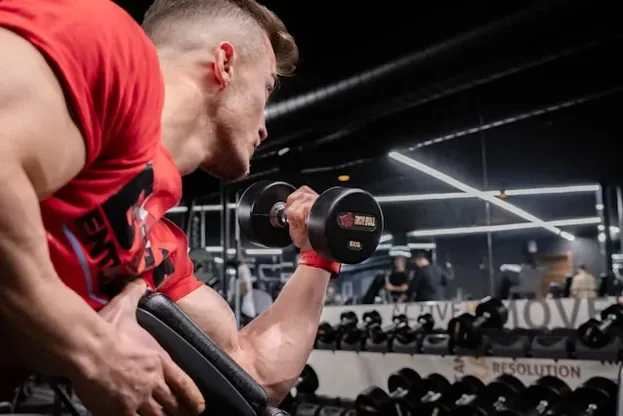Man in rood hemd die een bicepscurl met een halter uitvoert in de sportschool