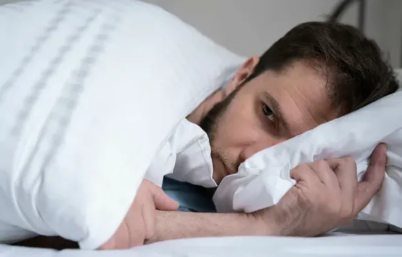 Man wakker in bed, ogen open, hoofd op het kussen