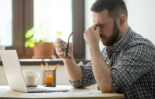 Vermoeide man achter zijn laptop, bril in de hand